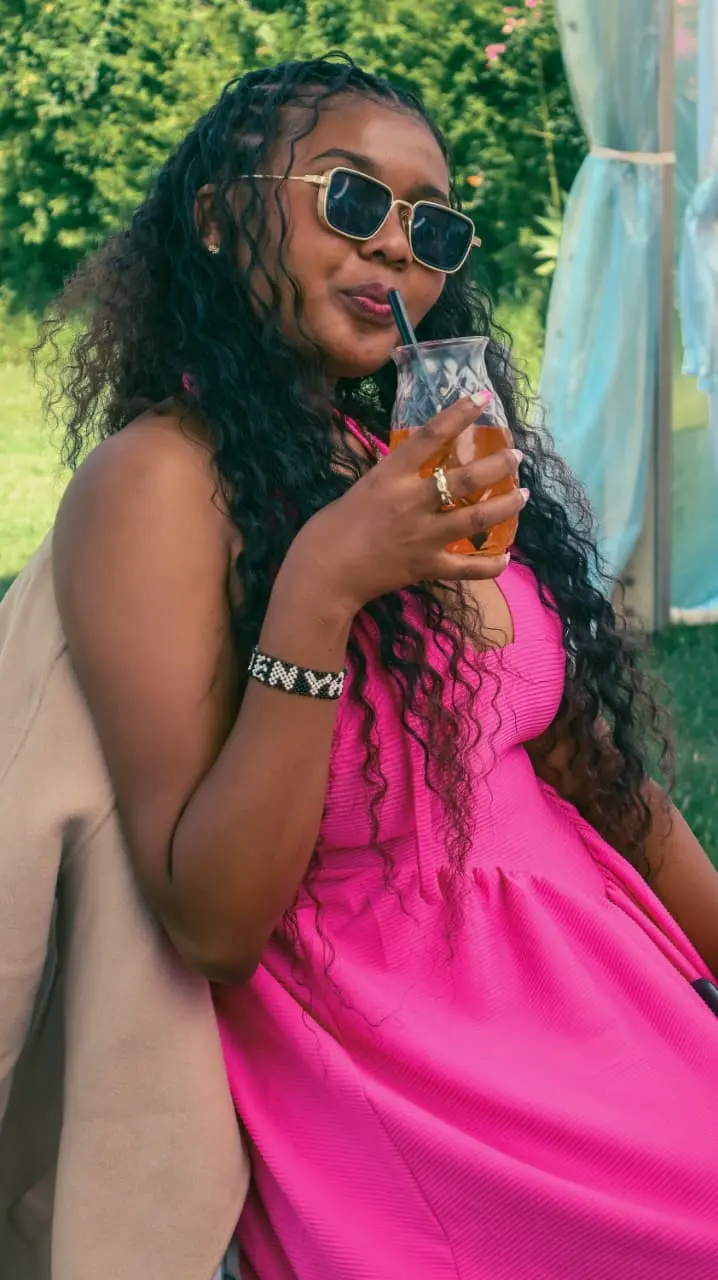 The same woman sipping a drink beneath a marquee, relaxed and smiling behind her sunglasses